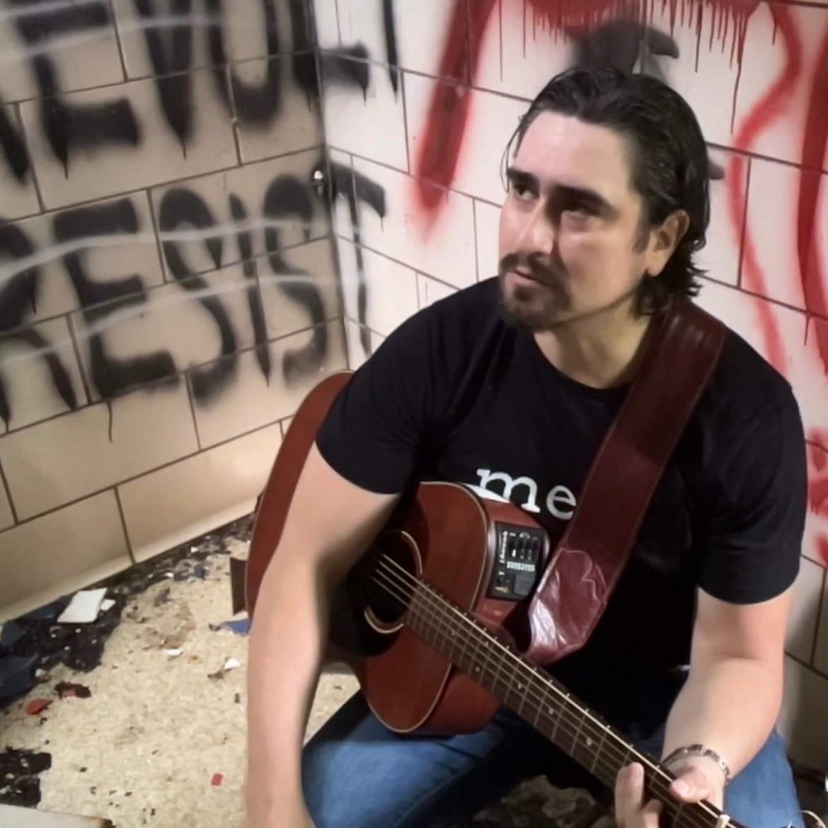 a man playing an acoustic guitar in front of graffiti